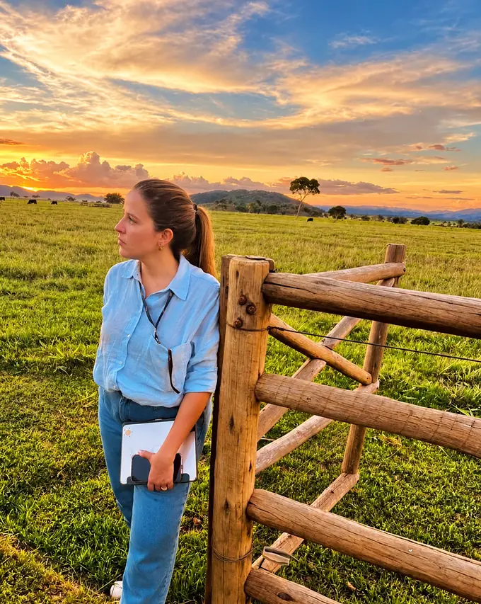 Raissa Curado na porteira de uma fazenda ao pôr do sol